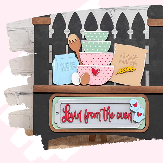 Janet's Craft Corner presents the "Lovin from the Oven Interchangeable Insert," a charming DIY decor kit featuring stacked bowls with polka dots and hearts, a wooden spoon, eggs, sugar, and flour packages against a brown fence. It includes an insert that reads "Love from the oven" adorned with hearts.