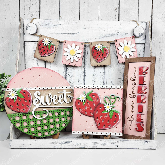 The Berry Sweet Decor Set from Janet's Craft Corner includes a wooden DIY craft kit featuring a "sweet" sign with strawberries and polka dots, a pink card with hearts, a rustic "Farm Fresh Berries" sign, and a strawberry-and-daisy garland on whitewashed wood—ideal for home decor.