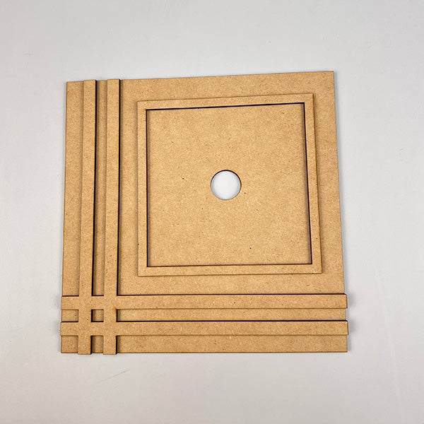 A Farmhouse Trim Interchangeable Squares Holder from Janet's Craft Corner, featuring decorative grooves, a circular center hole, and a design of parallel and perpendicular lines on two sides reminiscent of farmhouse trim, is displayed on a light-colored background.