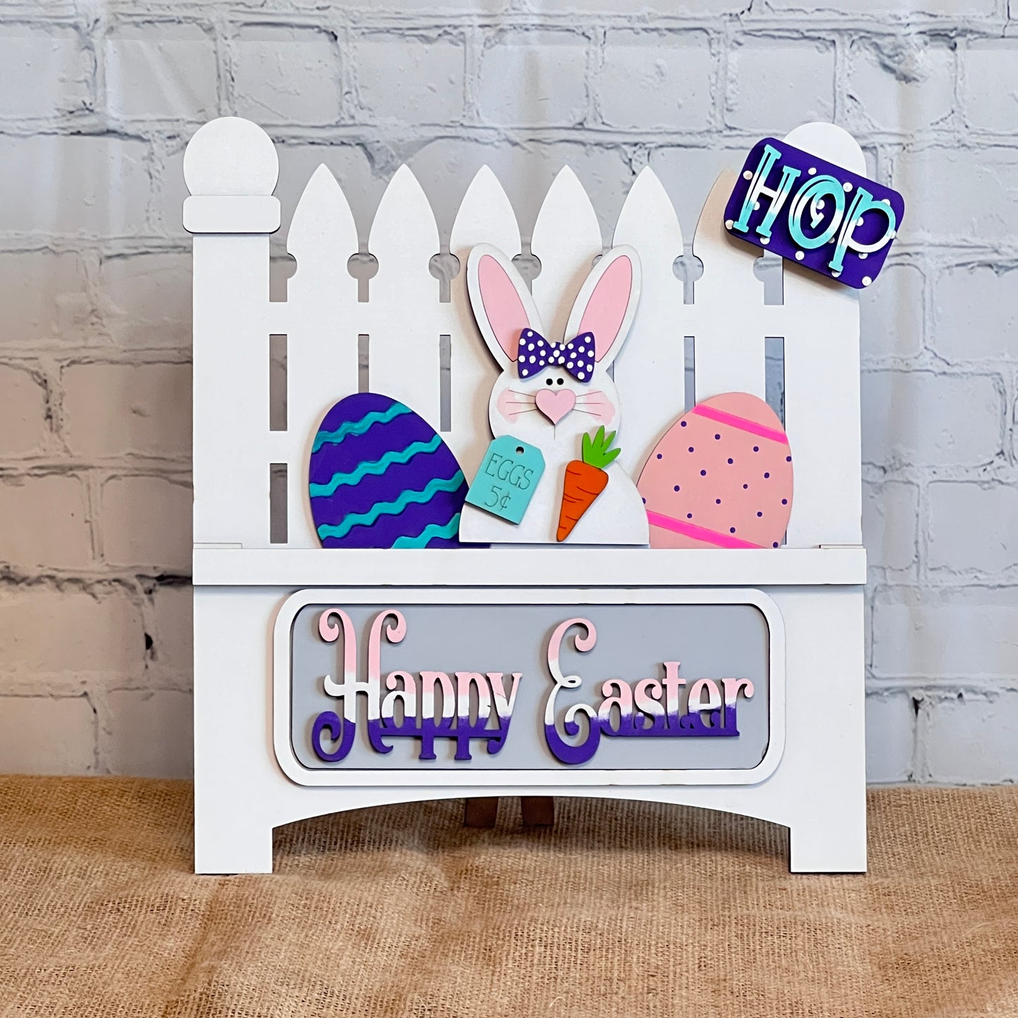 Janet's Craft Corner offers a DIY home decor kit: the Happy Easter Bunny Interchangeable Insert, featuring 3 pieces including a bunny with a carrot and "Eggs 5¢" sign, colorful eggs, and stylized "Happy Easter," perfect for decorating against a brick wall backdrop.