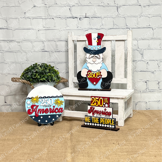 Janet's Craft Corner’s America 250 Mini Shelf Sitters, a DIY décor kit, features an Uncle Sam figure and patriotic signs like "250 Years America" and "We the People," displayed on a white tray with a small green plant for festive flair.