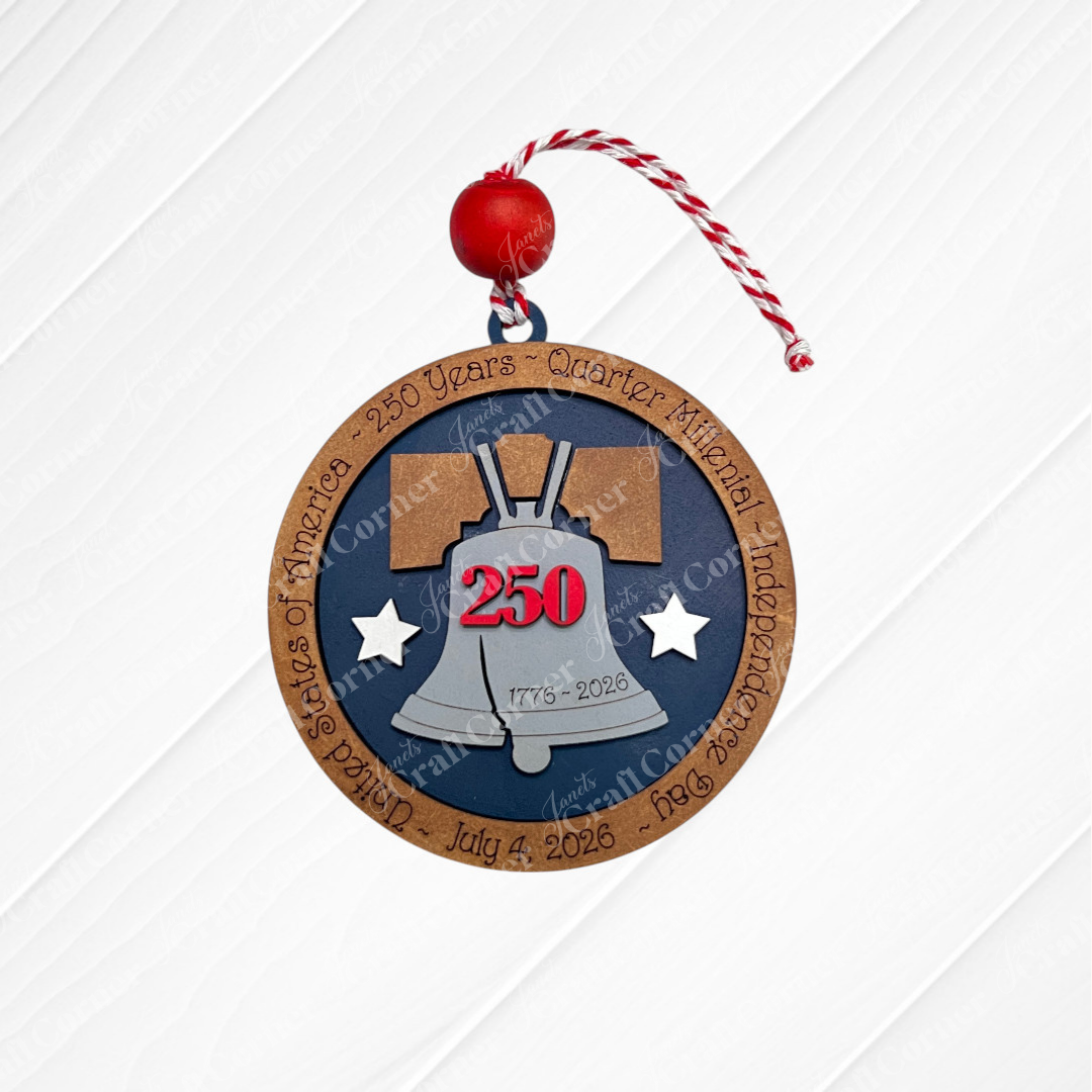 The Heartland America 250 Ornament - Painted is a round wood decoration with a red and white string, featuring a silver Liberty Bell, “250” in red, “1776-2026,” and the border reads “United States of America – 250 Years – Quarter America Independence Day – July 4, 2026.”.