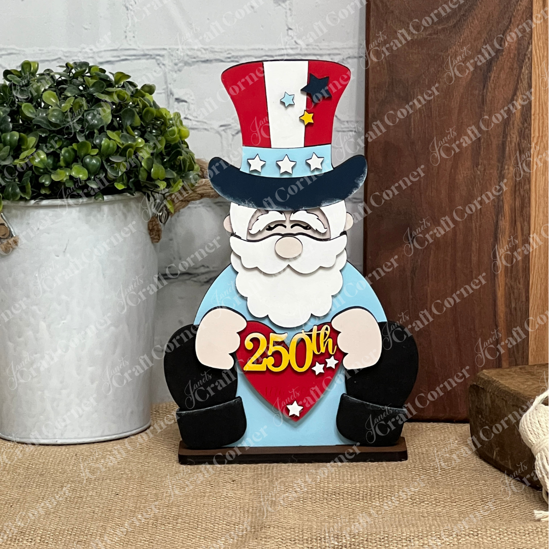The America 250 Mini Shelf Sitters DIY craft kit by Janet's Craft Corner features a wooden Uncle Sam with a red, white, and blue hat holding a "250th" heart with yellow stars—perfect patriotic décor for your table or tiered tray.