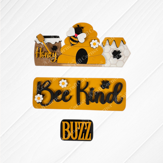 Introducing the Bee Interchangeable Insert - Painted from Janet's Craft Corner. This bee-themed wall decoration features a captivating beehive with a bee and honey pot, the phrase "Bee Kind" surrounded by delicate flowers, and the word "Buzz" against a stylish white patterned background. Customize your decor effortlessly with interchangeable craft inserts for any occasion.