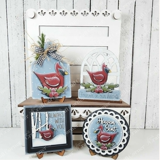The Cardinal Decor Set by Janet’s Craft Corner features your choice of four decorative plaques, each adorned with red cardinals and heartfelt sympathy messages. Beautifully displayed on a white chair and shelf with rustic and floral accents, this DIY home decor craft kit is a perfect memorial keepsake that adds warmth to your space against a white wooden wall backdrop.