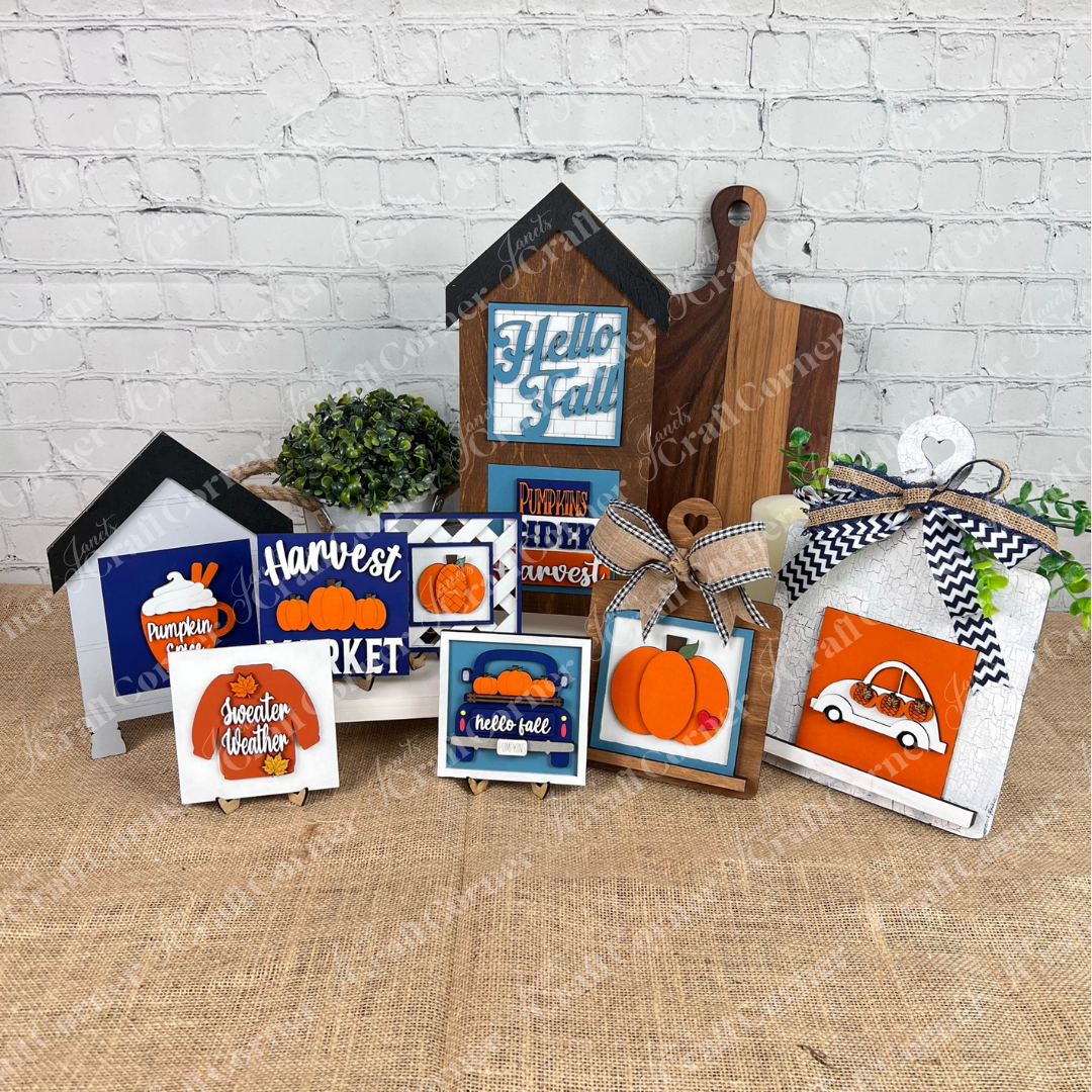 Janet's Craft Corner's Pumpkin Spice Squares are autumn-themed wood signs and tiered tray decor with pumpkins, fall leaves, and messages like "Hello Fall" and "Harvest Market," displayed on burlap against a white brick wall.