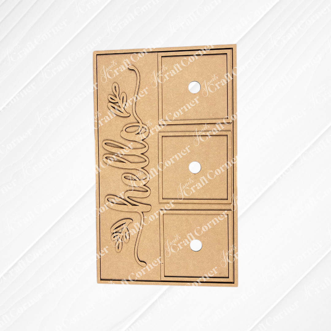 The Hello Swappable Squares Holder - DIY Craft Kit by Janet's Craft Corner is a brown, rectangular holder with three square cutouts, circular finger holes, and a cursive "hello" with a leaf—perfect for displaying seasonal inserts as shelf sitters.