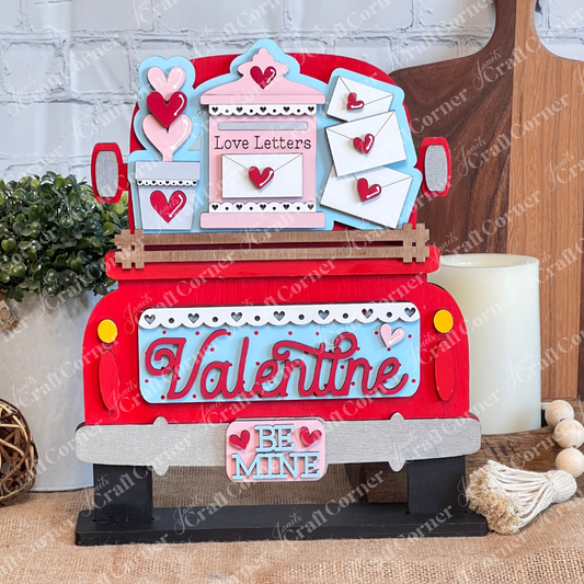 The Love Letters Interchangeable Insert by Janet's Craft Corner features a red truck with "Valentine," adorned with hearts and envelopes. With a "Love Letters DIY" sign and "Be Mine" below, it sits beautifully against a white brick wall and wooden cutting boards.