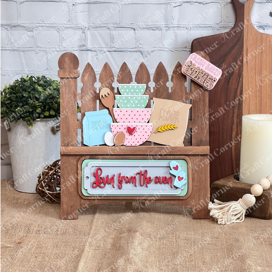 The Lovin from the Oven Interchangeable Insert by Janet's Craft Corner is a DIY home decor craft kit featuring a mini oven wooden sign with "Love from the oven" in red cursive, baking item cutouts, and a brick backdrop—perfect for home décor enthusiasts to add charm and creativity.