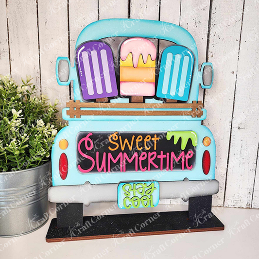 The Popsicle Interchangeable Insert from Janet's Craft Corner is a delightful DIY home decor kit featuring a decorative sign shaped like a vintage truck with colorful popsicles in the back. The tailgate is adorned with the phrases "Sweet Summertime" and "Stay Cool," complete with a small pot of green plants next to it. This charming piece makes a perfect addition to your home décor against its wooden background.