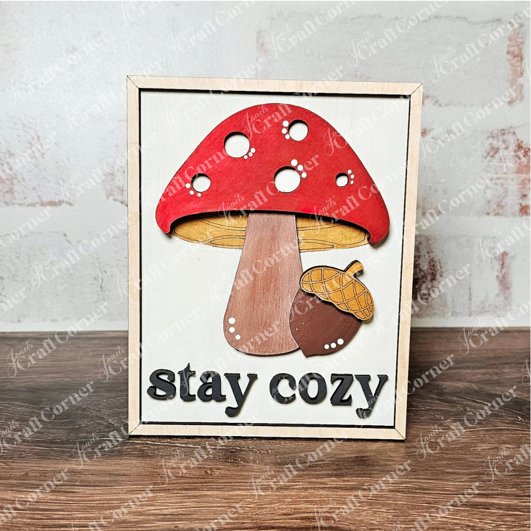 Janet's Craft Corner’s Fall in the Forest Switchable Farmhouse Sign DIY kit lets you create a charming woodland sign with a red and white mushroom, acorn, and “stay cozy” text—perfect for cozy seasonal home decor.