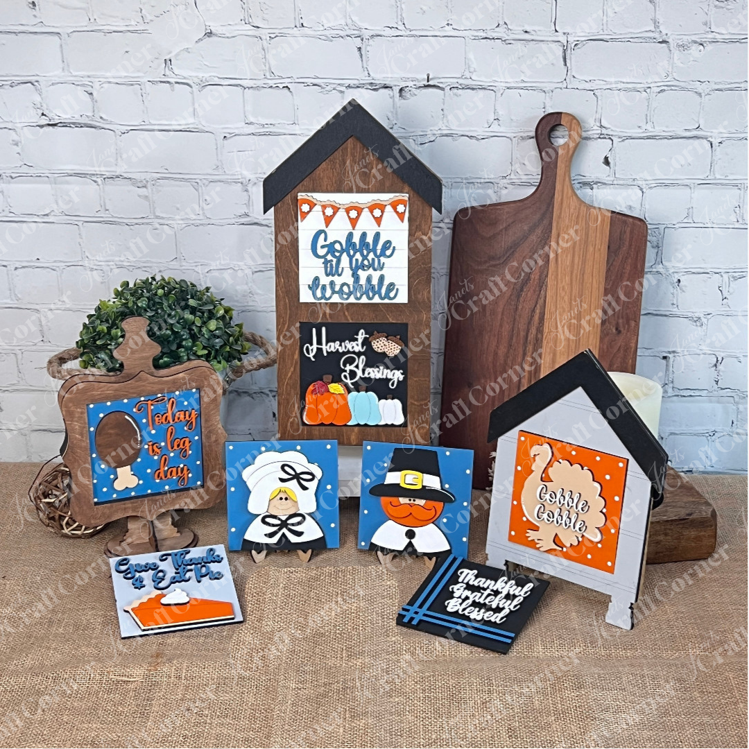 Janet's Craft Corner's "Thanksgiving Feast Squares"—festive wooden signs and cut-outs with turkeys, pumpkins, and hats—are displayed on burlap against a brick wall for a perfect holiday touch.