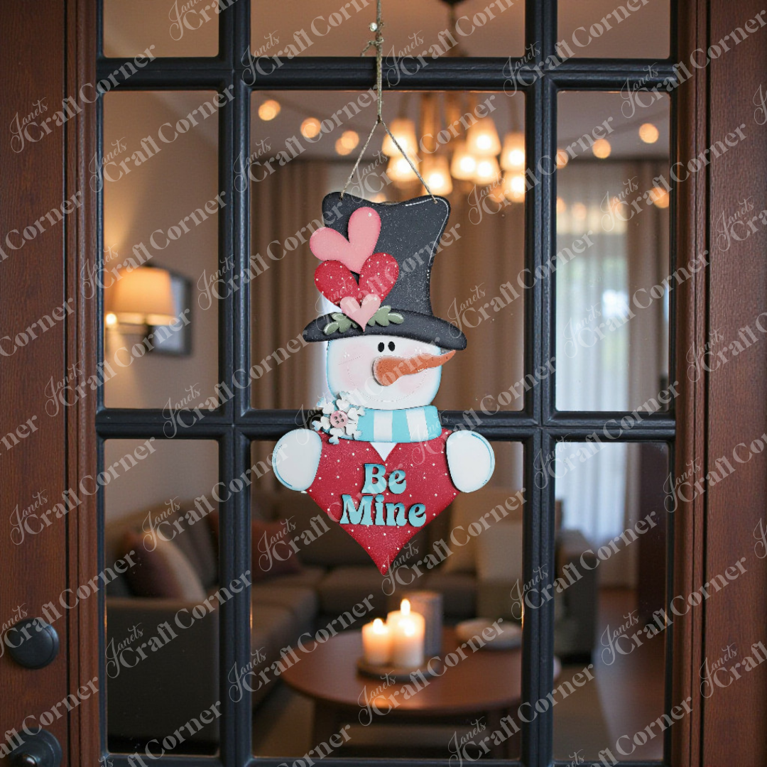 The Valentine Snowman Door Hanger DIY kit by Janet's Craft Corner features a snowman with a black hat, red hearts, and a "Be Mine" heart, adding charm to your entryway with cozy, seasonal decor. Set of 1.