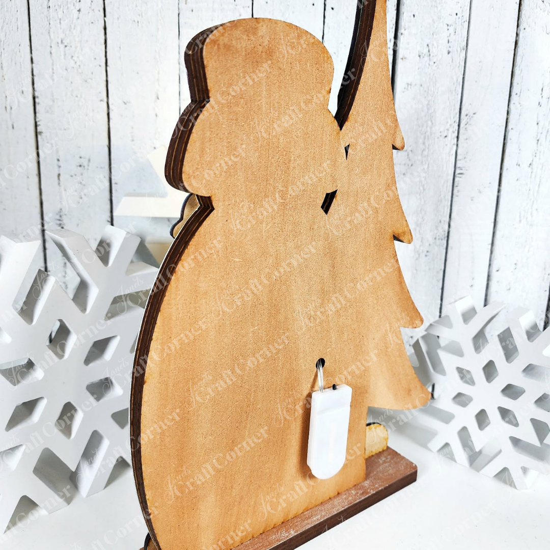 The Winter Snowman Shelf Sitter by Janet's Craft Corner is a DIY seasonal home decor kit featuring a wooden snowman and tree with a white hook and decorative snowflakes—perfect for festive winter displays on any shelf. Set of 1.