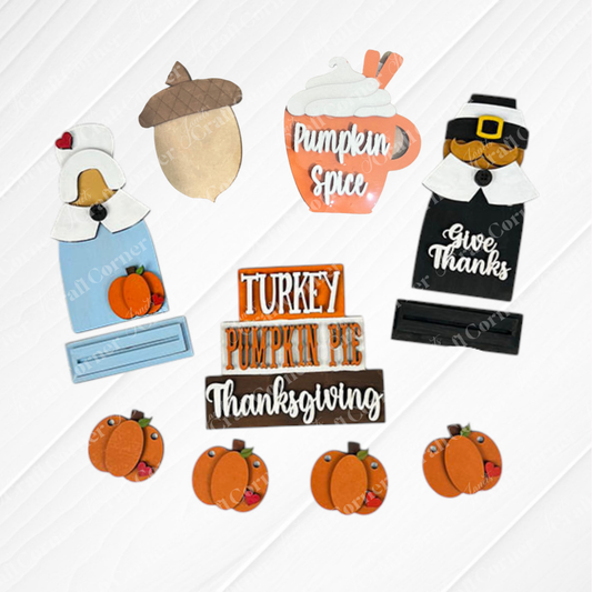 The Heartland Thanksgiving Tiered Tray – Painted includes assorted wooden cutouts for tiered tray decor, featuring a pilgrim, bonneted woman, pumpkins, acorn, pumpkin spice mug, and festive “Turkey” and “Give Thanks” signs.