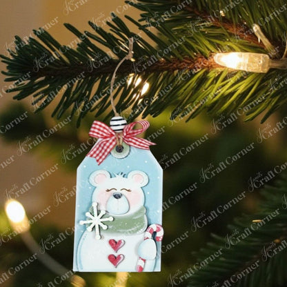 A Christmas tree branch holds a Janet's Craft Corner Forest Friends Ornaments kit bear tag, complete with scarf, snowflake, candy cane, red bow, and bell—one of five DIY craft kits available.