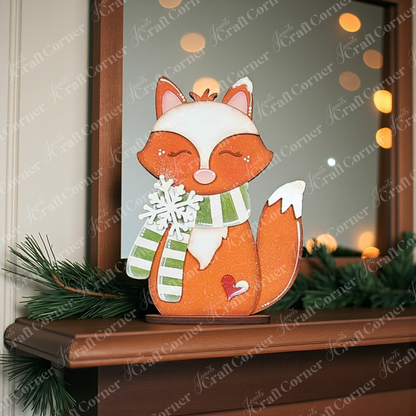 A Forest Friends Shelf Sitter from Janet's Craft Corner, wearing a green striped scarf, sits on a pine-adorned mantel with glowing bokeh lights—perfect woodland decor. DIY seasonal home craft kit; choose from 3 designs.