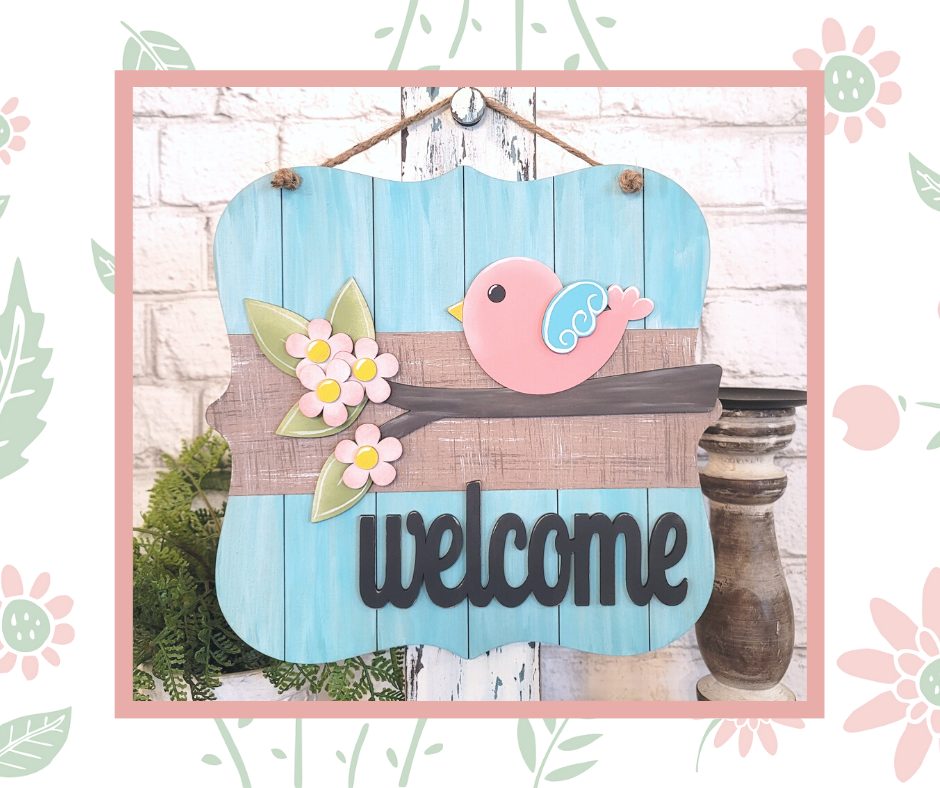 The Bird Welcome Sign from Janet's Craft Corner is a DIY seasonal home decor craft kit featuring a pink bird on a floral-branch against a blue wood backdrop, with "welcome" in bold black letters, perfect for adding charm to your entryway.