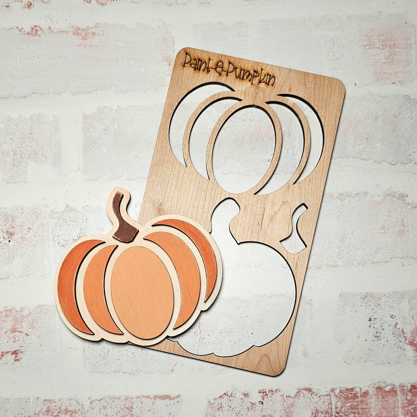 Introducing the Paint a Pumpkin Kids Pop-Out Kit by Janet's Craft Corner! This DIY craft kit includes a wooden pumpkin painting set with a stencil and cut-out pumpkin piece, ideal for enhancing your home décor. The stencil provides sections for both the pumpkin and its stem, all displayed on a white brick background. Get creative and add charm to any room by painting your own pumpkin masterpiece!