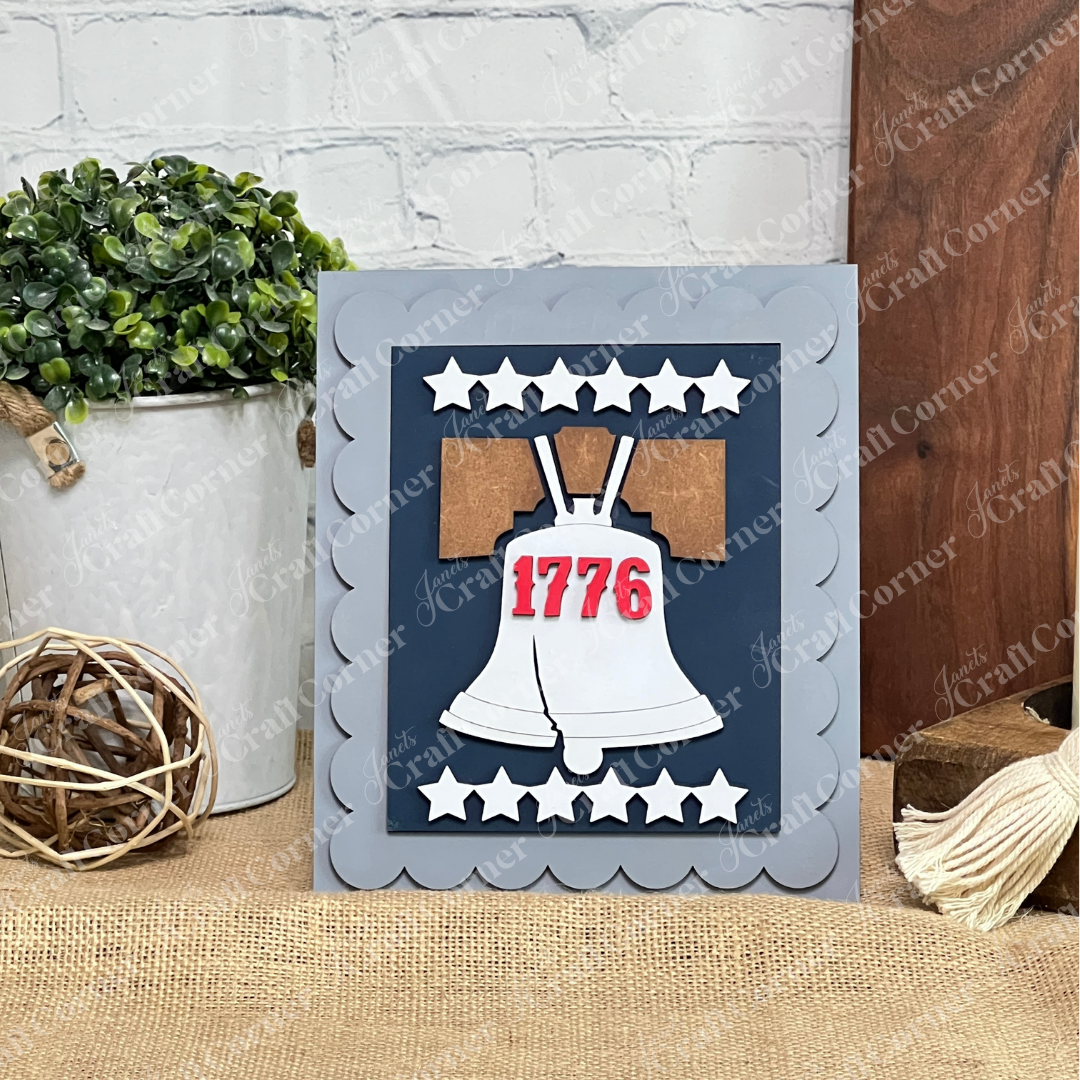 The Janet's Craft Corner Patriotic Farmhouse Signs DIY kit includes a handmade card with a white Liberty Bell and "1776" in red on a starry blue background—perfect for seasonal tiered tray decor or DIY farmhouse signs. Set of 1.