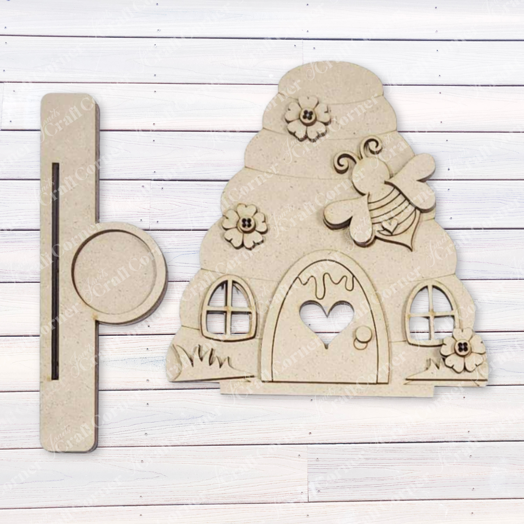 Introducing the Honey Bee Mini Shelf Sitter Set from Janet's Craft Corner, a delightful DIY craft kit. Adorned with flowers, a bee, and a heart on the door, this wooden beehive-shaped piece is perfect for bee-lovers. Comes in a set of three and makes charming seasonal home decor.