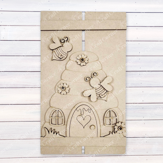Enhance your space with Janet's Craft Corner's DIY Beehive Pallet Sign Shelf Leaner. This wooden wall art features a carved beehive adorned with flowers, bees, and a heart-shaped door on a white slatted background, ideal for home decor enthusiasts.