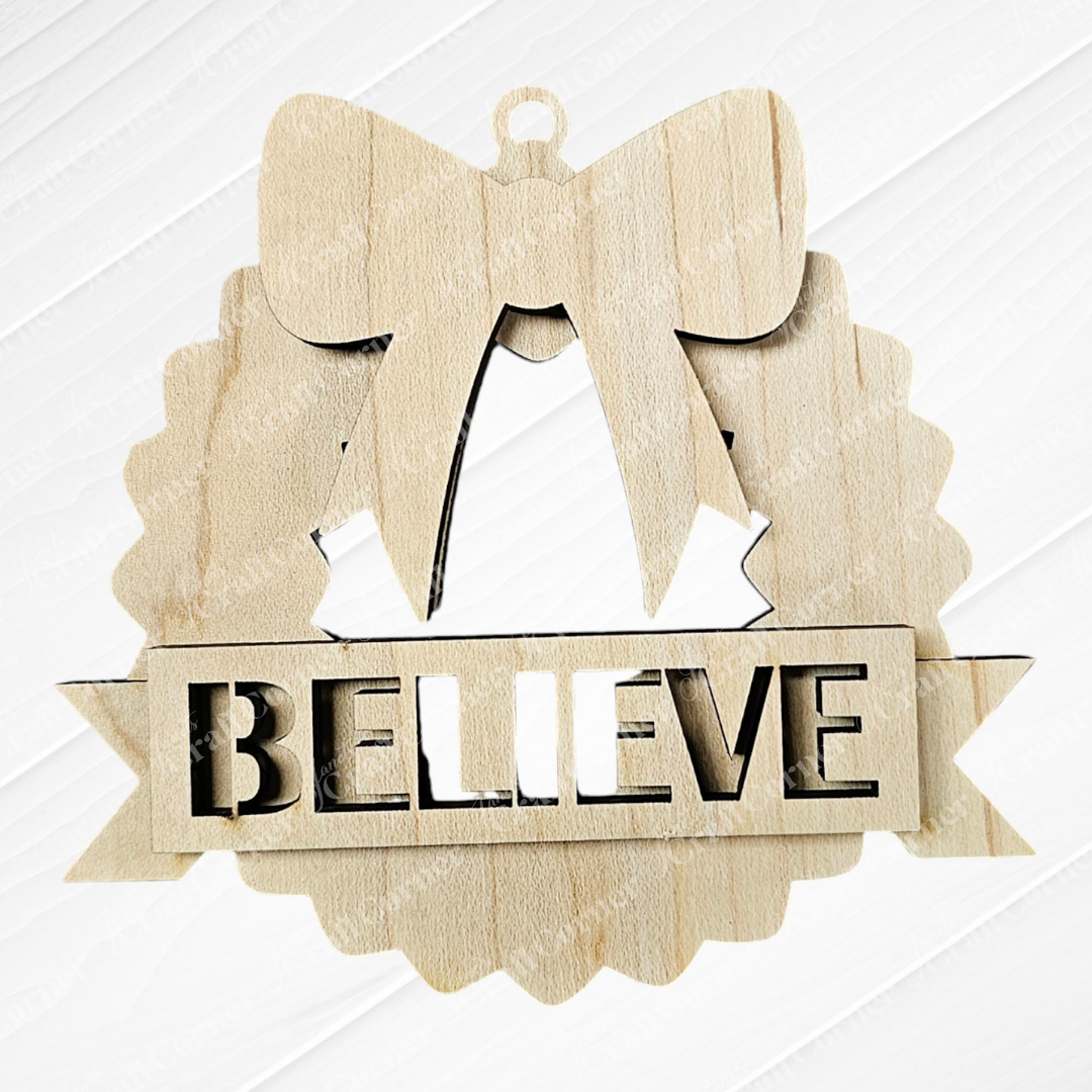 This hand-painted wooden Christmas ornament from Janet's Craft Corner showcases a wreath adorned with a bow at the top and the word "BELIEVE" prominently carved in the center. Its textured white background adds charm, making it an ideal addition to your Holiday Village Ornament Set - Early Access.