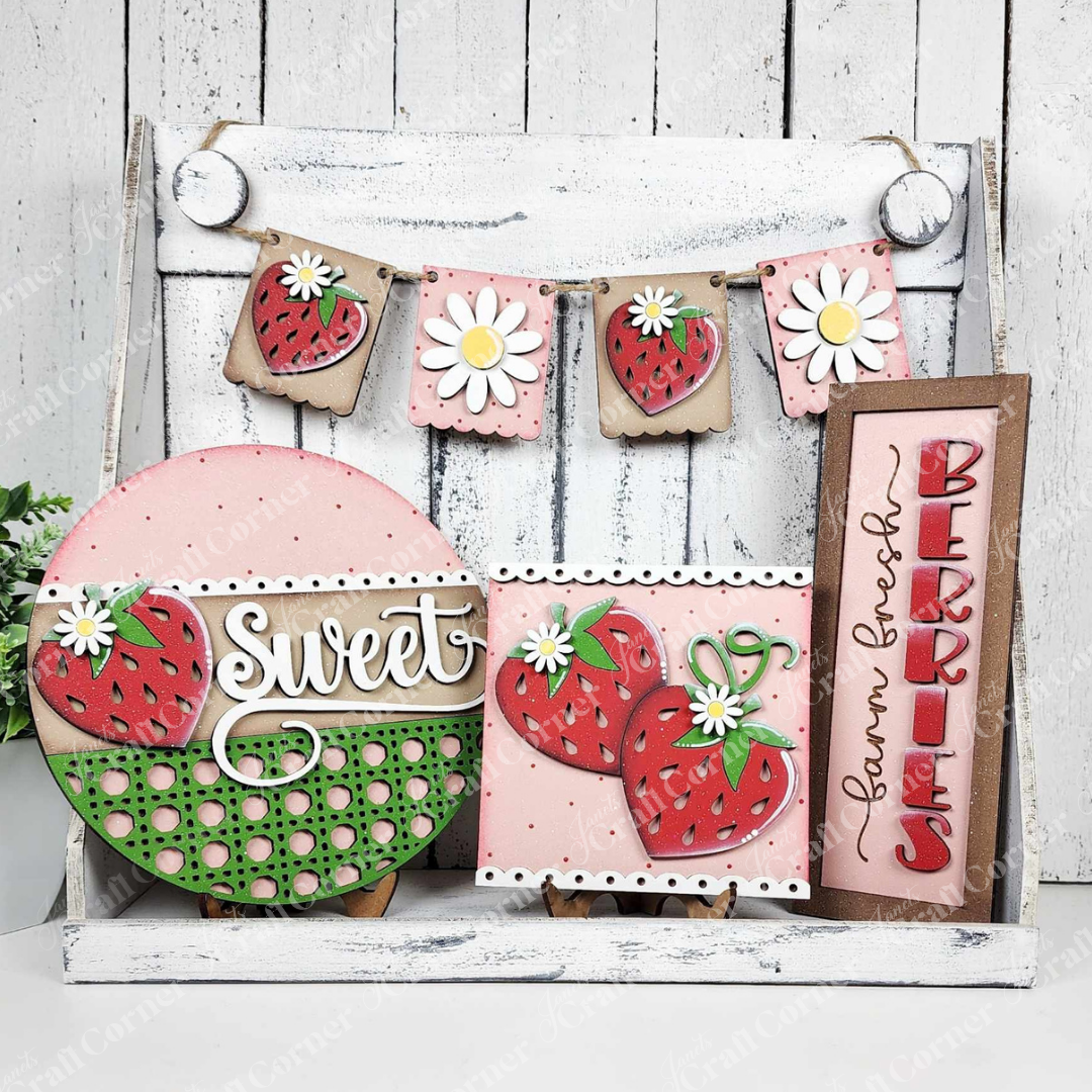 The Berry Sweet Decor Set from Janet's Craft Corner includes a wooden DIY craft kit featuring a "sweet" sign with strawberries and polka dots, a pink card with hearts, a rustic "Farm Fresh Berries" sign, and a strawberry-and-daisy garland on whitewashed wood—ideal for home decor.