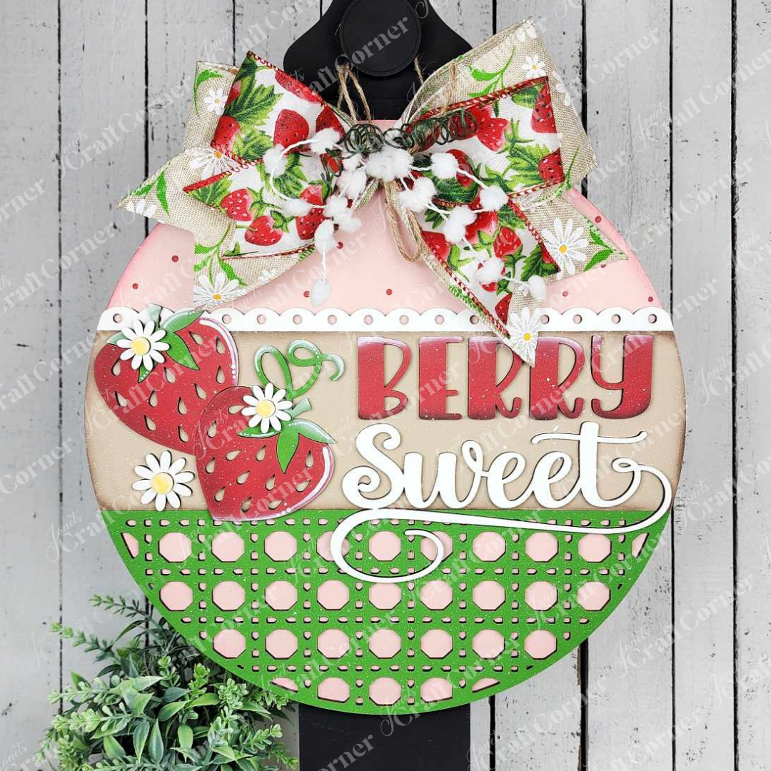 The Berry Sweet Wall Hanger by Janet's Craft Corner is a round decorative sign featuring strawberries, daisies, and "Berry Sweet" text in red and white against pink, beige, and green dotted sections with a strawberry-themed bow—ideal for charming home décor or as a DIY craft kit.