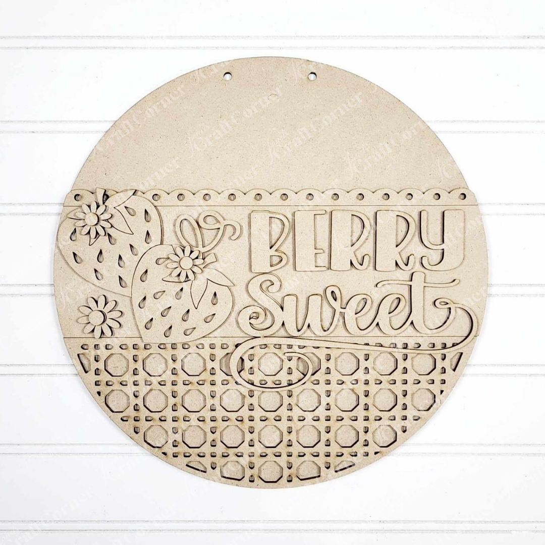 The Berry Sweet Wall Hanger by Janet's Craft Corner is a round wooden decoration with carved strawberries, flowers, and playful "Berry Sweet" text. The lower half features circular cutouts, placed beautifully on a white textured surface.