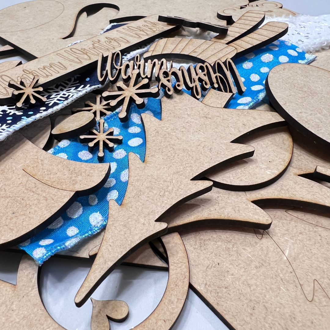 Laser-cut wooden craft pieces from Janet's Craft Corner's Crafted by You! Subscription are displayed on blue and black fabric—ideal for your craft kit or creative community, with new DIY home décor projects each month.