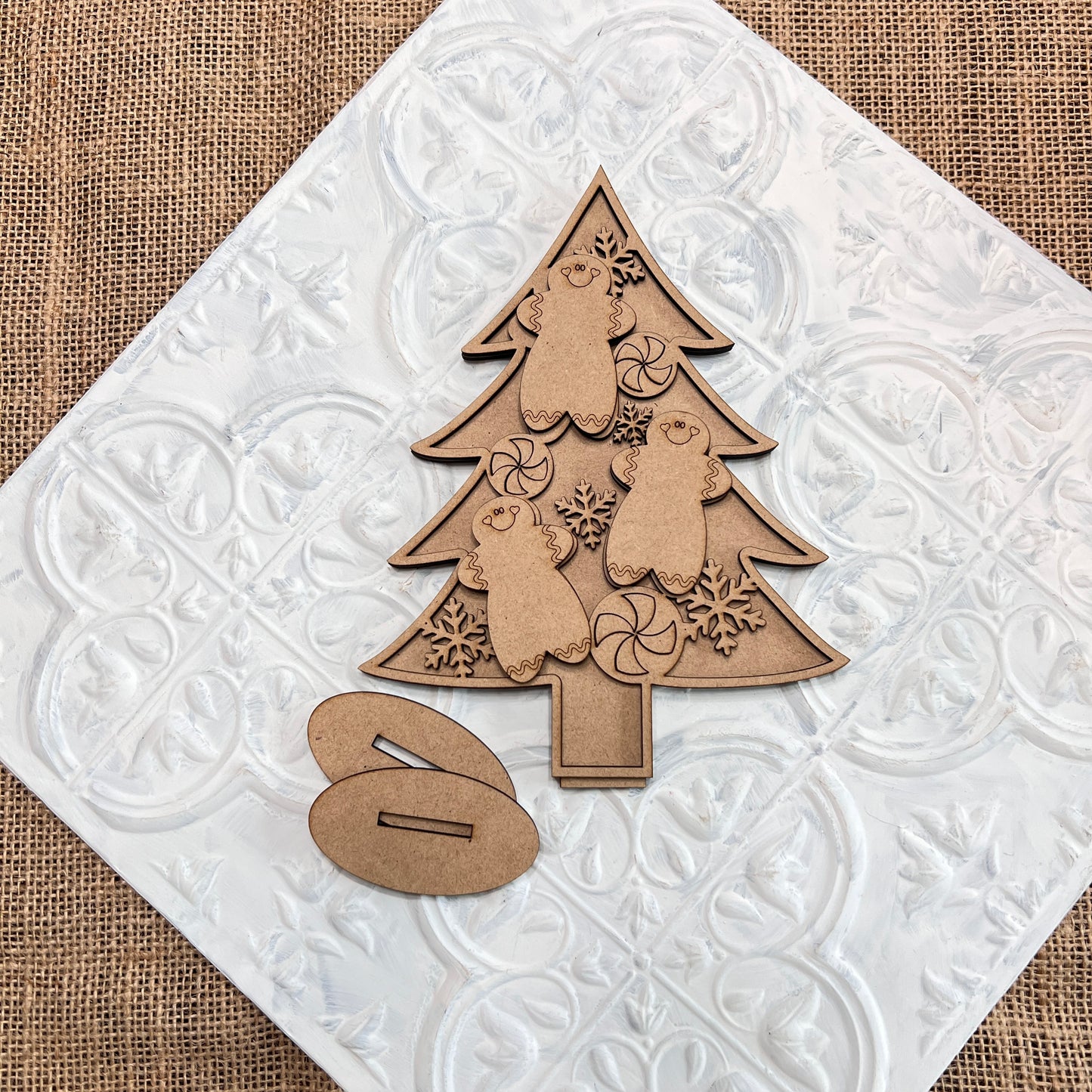 Capture the holiday spirit with Janet's Craft Corner's Standing Christmas Tree Shelf Sitters. These charming wooden ornaments, featuring intricate bear and snowflake cutouts, are set against a textured white tile background. A small wooden accent piece sits nearby on a burlap surface, making it an ideal choice for a festive shelf display.