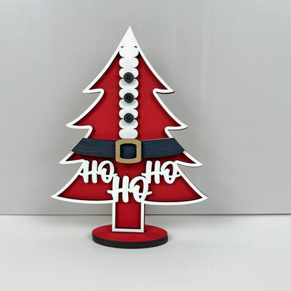 The Standing Christmas Tree Shelf Sitters from Janet's Craft Corner add festive charm to your holiday decor. Inspired by Santa's suit, they feature a red design with white trimming, black buttons, a black belt with a yellow buckle, and the words "Ho Ho Ho." Perfect for enhancing your shelf display this season.