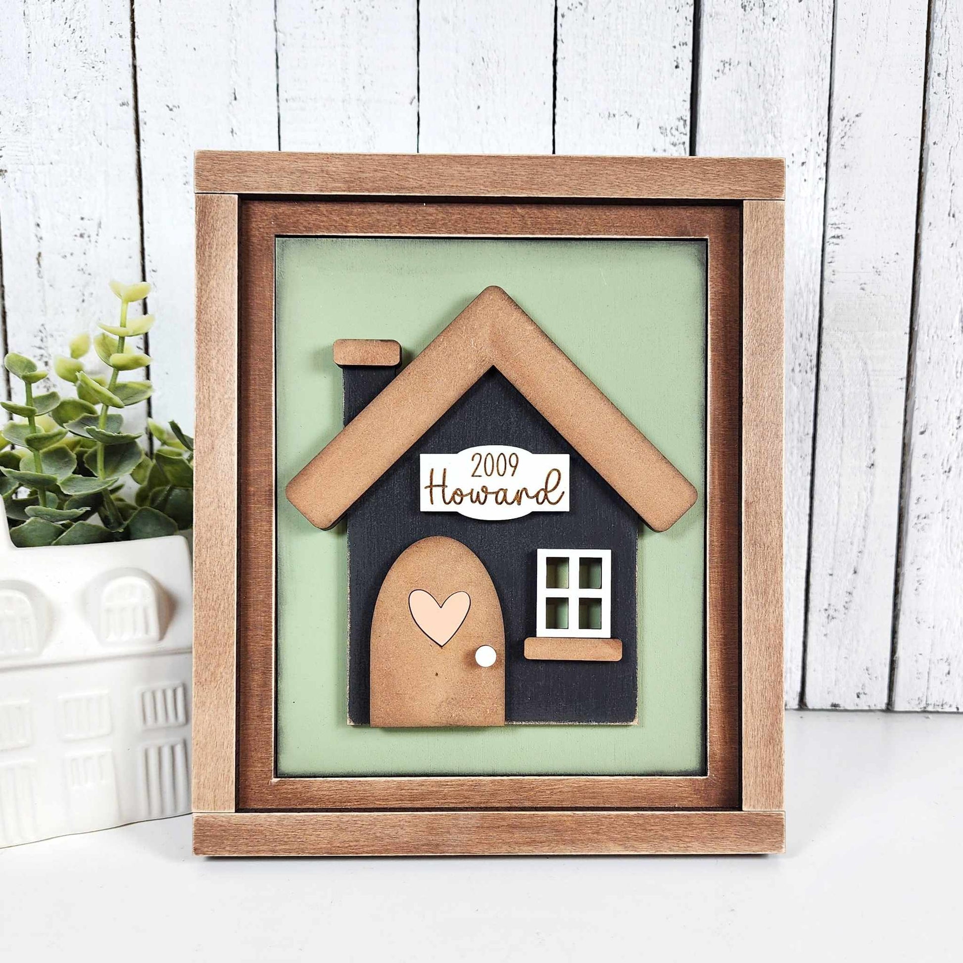 The Family-Home Switchable Farmhouse Sign by Janet's Craft Corner is a DIY home decor kit featuring "Howard," a small house with a heart on the door, "2009," and charming farmhouse accents—perfect for adding a personalized touch to your space.