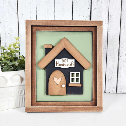 The Family-Home Switchable Farmhouse Sign by Janet's Craft Corner is a DIY home decor kit featuring "Howard," a small house with a heart on the door, "2009," and charming farmhouse accents—perfect for adding a personalized touch to your space.