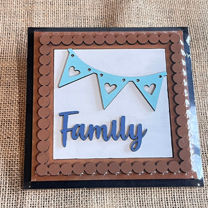 A handmade card with a brown scalloped border, blue heart pennant, and "Family" in blue script on white burlap—perfect inspiration for the Heartland Bead Trim Swappable Squares Frame with Inserts - Painted.
