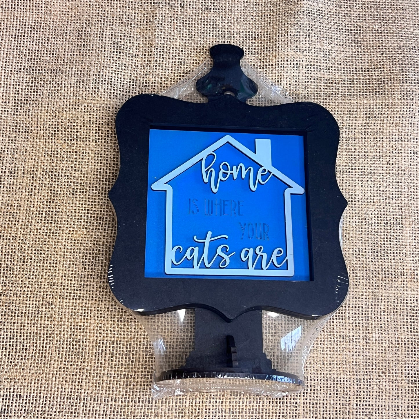 The Heartland Drop In Swappable Squares Holder is a house-shaped, decorative wood display with a black frame, blue background, and the phrase "Home is where your cats are"—a perfect DIY craft kit for cat lovers.