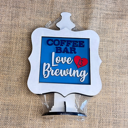 The Heartland Drop In Swappable Squares Holder DIY Craft Kit is a charming wood display with a white frame and base, perfect for coffee nooks. Add your own decorative signs to customize your space! Set of 1.