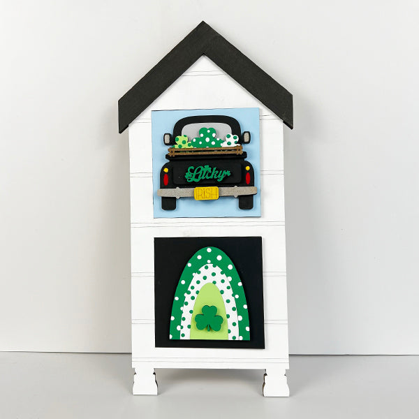 The House Swappable Squares Holders Shelf Leaner DIY Craft Kit by Janet's Craft Corner features a decorative white wooden house with a black roof, shamrock truck and rainbow designs, adding farmhouse charm to your decor.