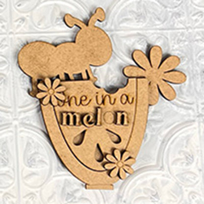 A charming wooden cutout from Janet's Craft Corner, shaped like a slice of watermelon with a bee on top, makes an ideal addition to farmhouse decor. Adorned with the text "one in a melon" amid decorative flower patterns, this piece is similar to the Watermelon Shelf Sitters and rests beautifully against a textured white surface.