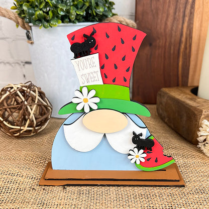 The "Watermelon Shelf Sitters" by Janet's Craft Corner serve as the perfect centerpiece for farmhouse decor with their whimsical wooden figure. This character boasts a blue figure, a white beard, and a charming watermelon-themed top hat. Complemented by a "You're Sweet" sign, daisies, and tiny black ants, these elements harmonize beautifully with the burlap backdrop, making it an ideal addition to any rustic space.