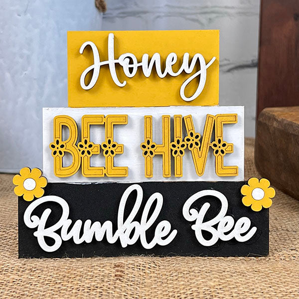 This delightful farmhouse-style decor from Janet's Craft Corner, part of their Summer Word Stacks collection, includes stacked decorative signs: "Honey" elegantly scripted on a yellow background, "Bee Hive" embellished with bee and hive motifs on white, and "Bumble Bee" in cursive on black featuring yellow flowers framing each side—ideal for summer word stacks or DIY kits.