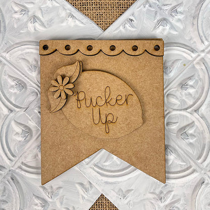 Introducing the "Pucker Up" wooden banner from Janet's Craft Corner—a delightful lemon-shaped design accented with a flower. Ideal for summer mini signs, this piece features a scalloped edge with convenient hanging holes. The background boasts a textured pattern in white and beige, making it a perfect addition to your home decor collection.