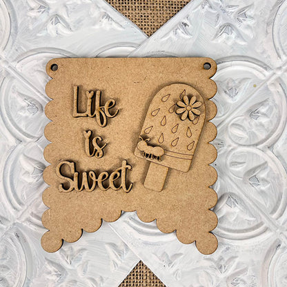 From Janet's Craft Corner, the Summer Mini Signs collection features a charming decorative wooden sign with scalloped edges and the phrase "Life is Sweet." Accompanying the text is a popsicle embellished with raindrop shapes and a flower, all set against a textured white and burlap background, making it an inviting piece of home decor.