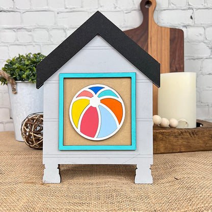 The House Swappable Squares Holders Shelf Leaner DIY Craft Kit by Janet's Craft Corner features a decorative house-shaped display with a beach ball design, set against neutral decor like plants and candles for a farmhouse touch.