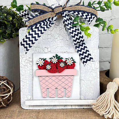Add a pop of color to your space with Janet's Craft Corner Breadboard Swappable Squares Holder DIY Craft Kit—a square sign featuring a pink flower pot with red strawberries, white flowers, and greenery on a rustic background.