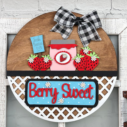 Introducing the "Berry Sweet Interchangeable Insert" from Janet's Craft Corner, a delightful DIY home decor kit. This charming farmhouse piece combines strawberries, a heart-shaped jar, and a "Fresh Berries 25¢" label. The phrase "Berry Sweet" stands out in red on blue with white daisies, complemented by a black and white checkered bow at the top.