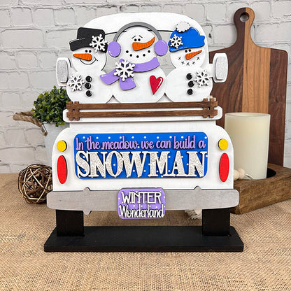 From Janet's Craft Corner, the Snowman Interchangeable Insert is a DIY home decor kit that features a charming white truck decorated with snowmen and snowflakes. It includes the phrases "In the meadow we can build a SNOWMAN" and "Winter Wonderland." This versatile piece sits beautifully on a burlap-covered surface accompanied by a candle and branch, making it ideal for adding seasonal flair to your space.