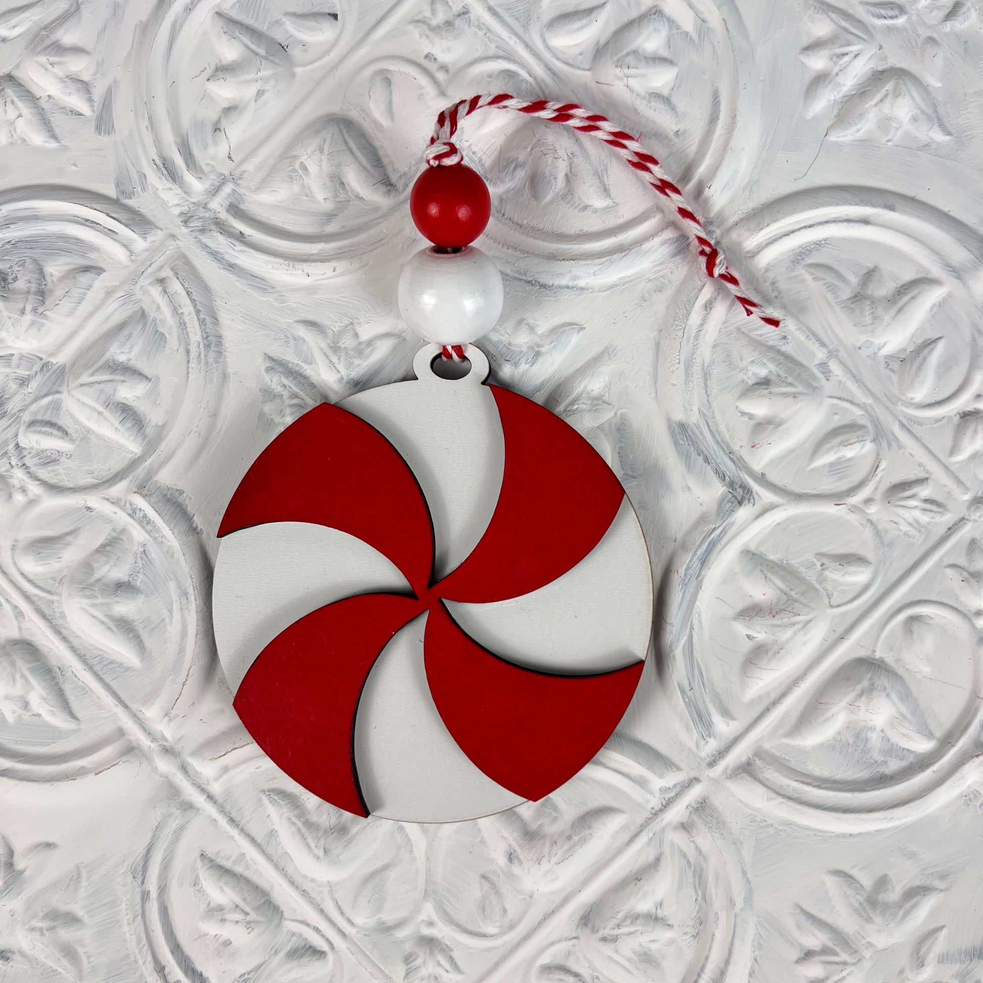 Introducing the Round Christmas Ornaments from Janet's Craft Corner! These DIY Decoration Kits feature red and white swirled ornaments adorned with two beads and a red and white twisted string, all set against a textured white backdrop. Perfect for adding festive charm to your holiday decorations.