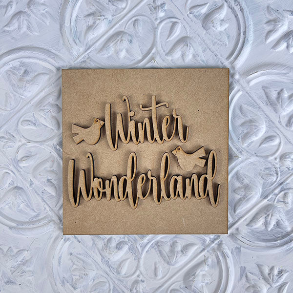 Janet's Craft Corner presents "Winter Interchangeable Squares" featuring wooden cutout text of "Winter Wonderland" with bird shapes, ideal for tiered trays and showcased on a decorative textured background.